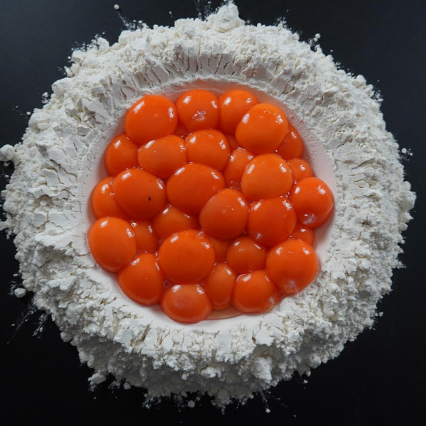 Photo of orange yolks on top of a pile of flour 