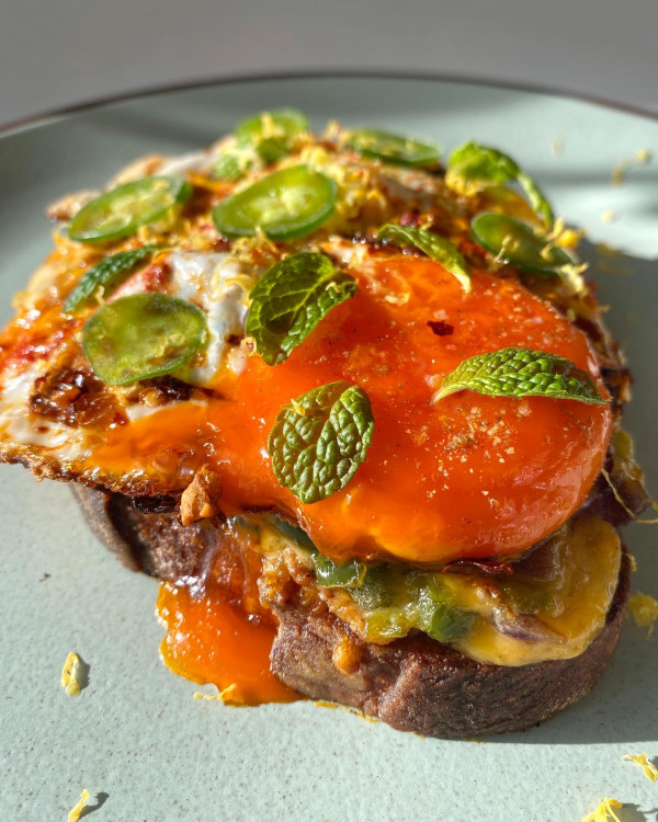 Photo of sourdough toast topped with mustard, red onion, jalapeno and cheese, with a fried Happy Egg on top
